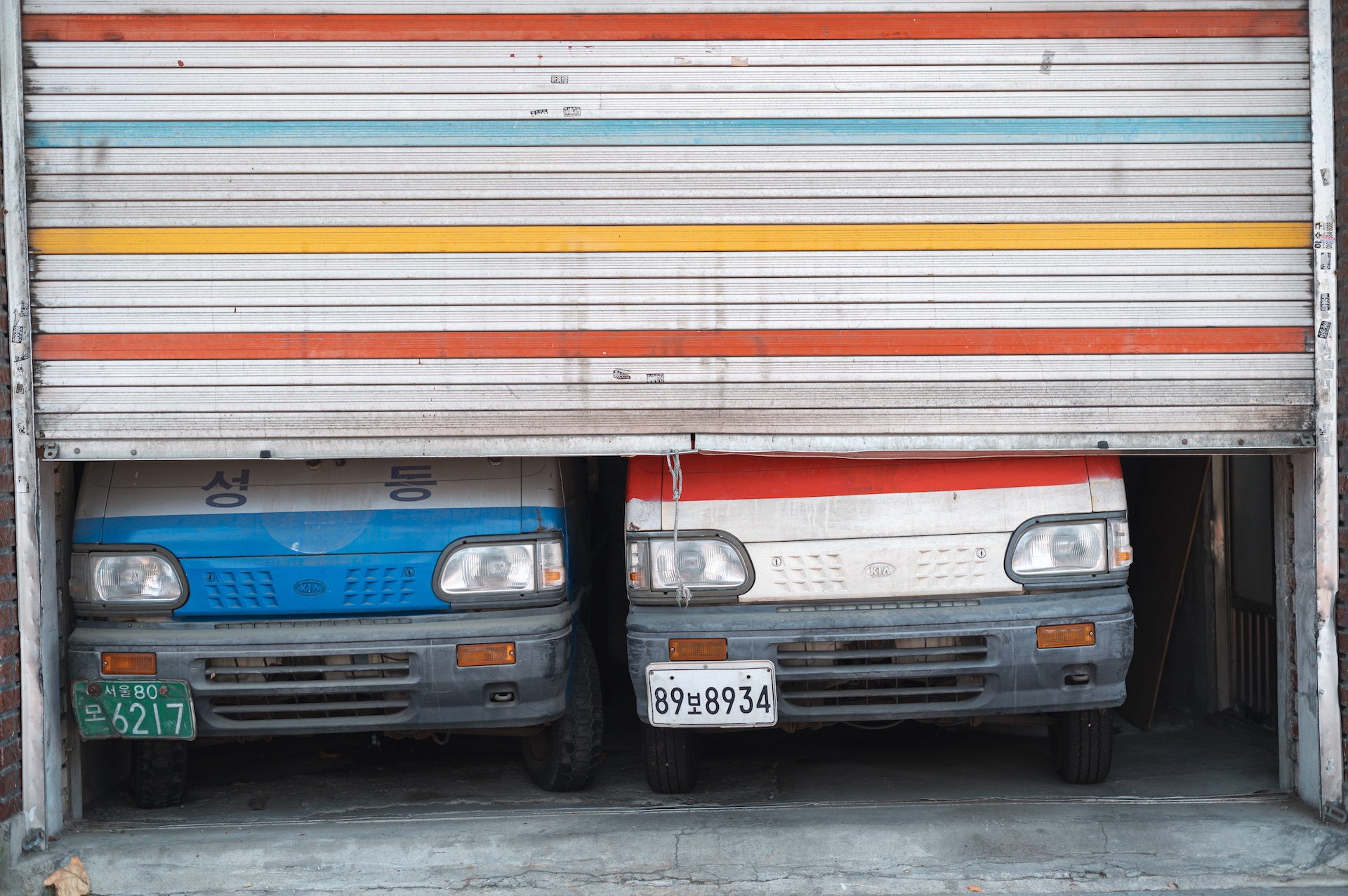Two Korean Damas vans peeking under a colorful shutter of a small business in Seoul, South Korea